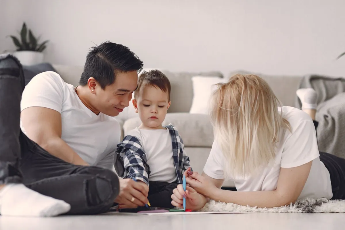 Eltern und Kind malen gemeinsam auf dem Boden, Sinnbild für Familienabsicherung über Generationen